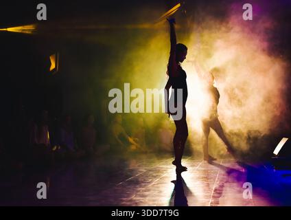 Dancers move gracefully demonstrating energy while performing on a dark stage with smoke Stock Photo