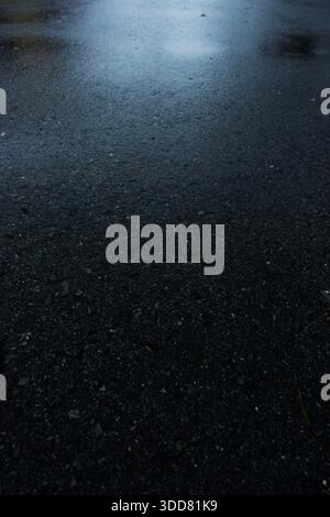 Rain-soaked asphalt road surface with subtle reflections, creating a dark, moody urban texture background. Stock Photo