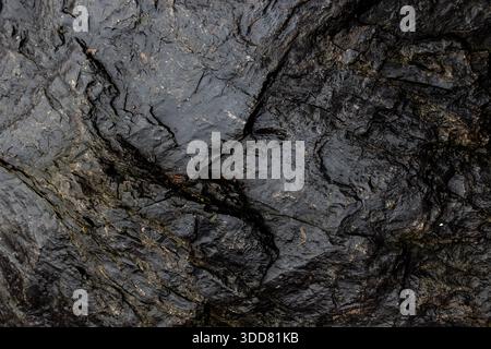 Close-up of dark natural stone with golden mineral veins, showing rugged texture and geological details Stock Photo