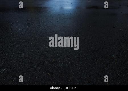 Rain-soaked asphalt road surface with subtle reflections, creating a dark, moody urban texture background. Stock Photo