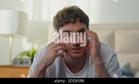 Cheerful smiling Caucasian young man guy talking on smartphone in bedroom at home happy European business male laughing mobile phone call speaking Stock Photo