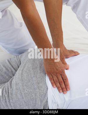 A woman is being massaged by a man. The woman is laying on a bed and the man is massaging her back. The man is using his hands to massage the woman's Stock Photo