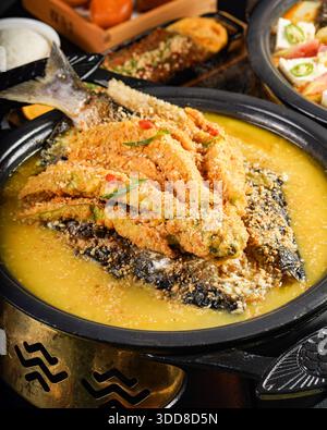 Appetizing fried fish dish presented in a bowl, topped with crispy batter and herbs, served with a side of savory sauce Stock Photo