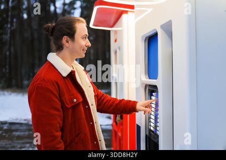 Young man in red winter jacket using outdoor vending machine kiosk in snowy park. High quality photo Stock Photo
