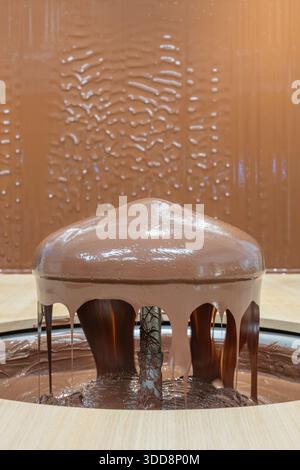 A glossy dome of melted chocolate cascades from a chocolate fountain, dripping into a pool on a light wooden surface. Rich, indulgent dessert display Stock Photo