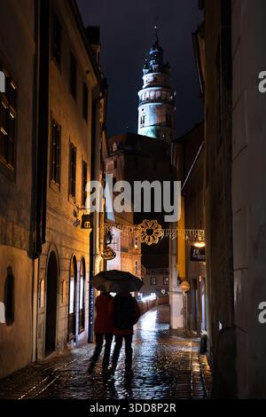 Rainy Night in Cesky Krumlov with Two People Walking and Castle Tower in the Background, Cesky Krumlov, Czech Republic. Stock Photo