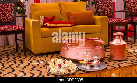 Copper vessels and floral decorations arranged around a yellow sofa with cushions in a festive Hindu wedding setting. Stock Photo