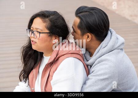 Multiethnic asian couple on a romantic moment talking while sitting on a park Stock Photo