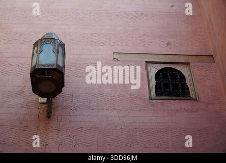 Textured pink wall with oriental wall lantern and small arched window protected by a wrought iron grille, traditional architectural ambiance. Stock Photo