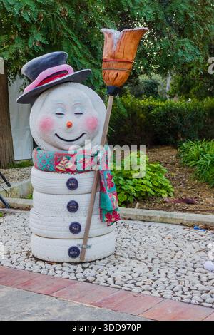 Whimsical Snowman Sculpture With Top Hat, Broom, And Floral Scarf In Garden Display Stock Photo