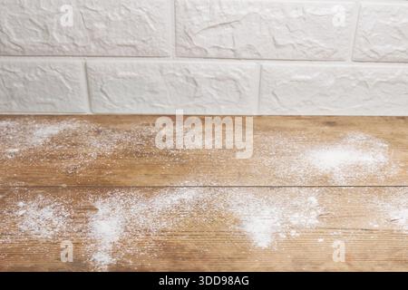 Wooden kitchen table with scattered flour against white brick wall Stock Photo