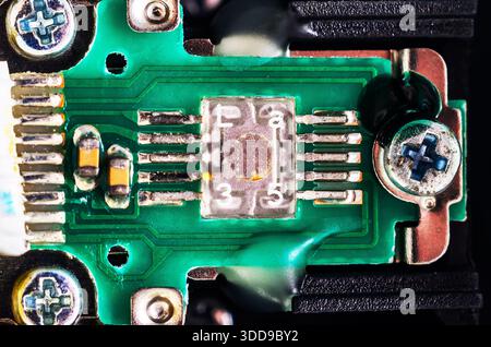 Extreme close-up of a surface-mount component on a green circuit board with screws Stock Photo
