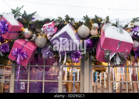Moscow, Russia, 29 December 2025, A close-up of a Christmas market stall decoration featuring large purple and pink gift boxes with bows hanging among Stock Photo