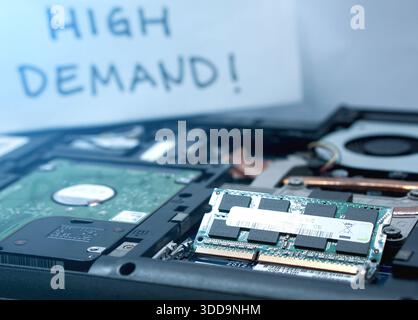 A laptop RAM chip in sharp focus with a "High Demand" sign blurred in the background. Conceptual image for the rising cost, scarcity, and importance o Stock Photo