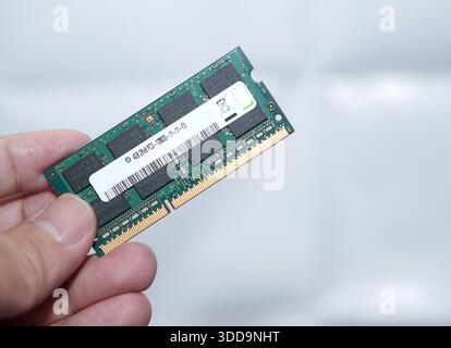 A clear, isolated shot of a user holding a green PCB RAM stick. Focuses on the memory chips and gold connector pins against a simple white backdrop. Stock Photo