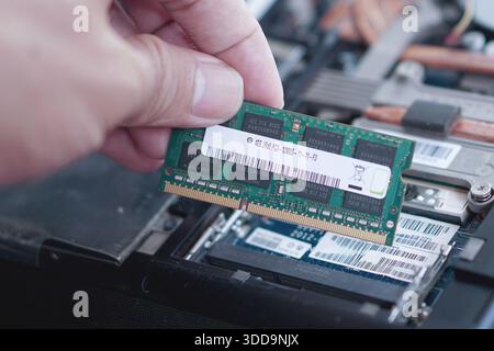 A hand holding up a laptop memory stick to show the product label and specifications against a background of computer internals. Stock Photo