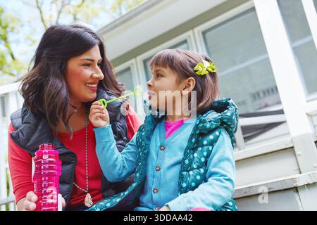 Mom, girl and blow bubbles in backyard, happy and play with care, love and bonding with connection. People, mother and daughter with soap bottle Stock Photo