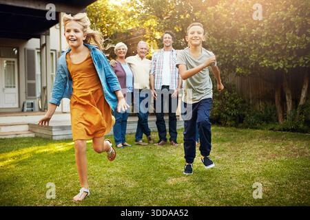 Family, children and smile with running in backyard for playing together, bonding or weekend break. Happy kids, generations and siblings with energy Stock Photo