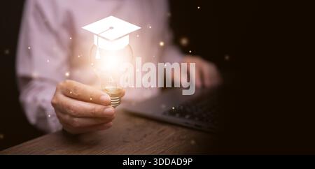 A man with his laptop holding glowing lightbulb with graduation cap. Online digital education, e-learning, self learn, improvement, and development, k Stock Photo