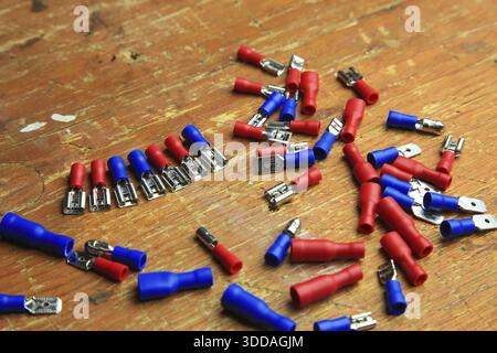 Red and blue insulated crimp and flat connectors (male and female) are scattered on a wooden surface. Visible metal contacts and open ends indicate wo Stock Photo