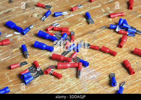 Red and blue insulated crimp and flat connectors (male and female) are scattered on a wooden surface. Visible metal contacts and open ends indicate wo Stock Photo
