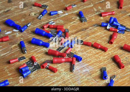 Red and blue insulated crimp and flat connectors (male and female) are scattered on a wooden surface. Visible metal contacts and open ends indicate wo Stock Photo