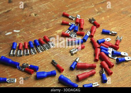 Red and blue insulated crimp and flat connectors (male and female) are scattered on a wooden surface. Visible metal contacts and open ends indicate wo Stock Photo