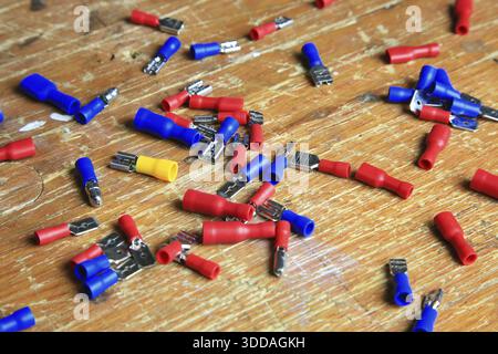 Red and blue insulated crimp and flat connectors (male and female) are scattered on a wooden surface. Visible metal contacts and open ends indicate wo Stock Photo