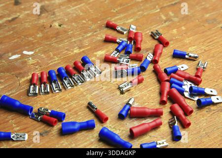 Red and blue insulated crimp and flat connectors (male and female) are scattered on a wooden surface. Visible metal contacts and open ends indicate wo Stock Photo