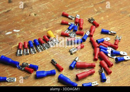 Red and blue insulated crimp and flat connectors (male and female) are scattered on a wooden surface. Visible metal contacts and open ends indicate wo Stock Photo