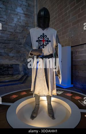 Alcantara, Spain - 10 June 23: A medieval knight in full armor displayed in a museum, wearing a chainmail and a tunic with a decorative emblem, standi Stock Photo