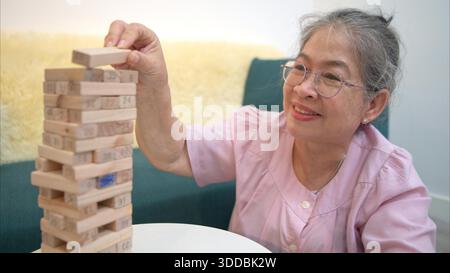 On a holiday, an elderly man enjoys jenga game in living room of house || Model released Stock Photo