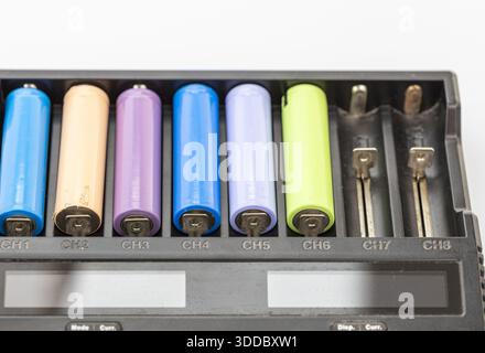 Close-up of a black battery charger with several colorful rechargeable batteries inserted in channels 1 through 6, the final two are vacant. White bac Stock Photo