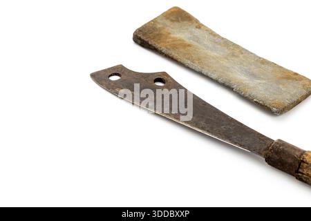 On white, a vintage rusty cleaver with a wooden handle lies next to a sharpening stone. Both show signs of age. The composition is simple, highlightin Stock Photo