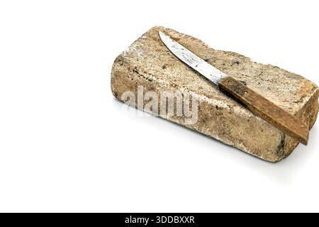 A slightly rusted metal knife with a wooden handle laying on a big thick whetstone in a studio shot. The composition is simple, with a white backgroun Stock Photo