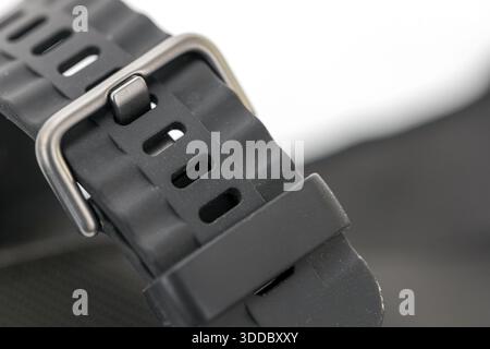 A close-up of a black rubber watch strap with a metal buckle on a white background. The strap has oval holes for adjustment and a matte finish. The bu Stock Photo