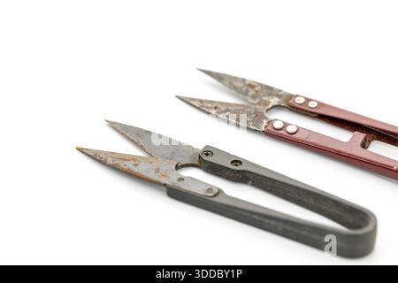 Two rusty Crab claw scissors lay diagonally on a white background. One has red handles, the other is black.  The snips are well-used and show wear. Sh Stock Photo