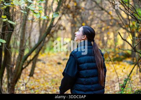 Young woman hiker with curly hair and backpack walking in forest during autumn, enjoying hiking and exploring nature Stock Photo