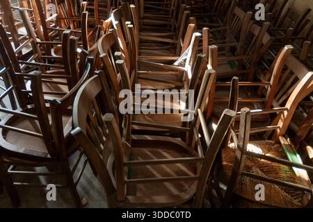 Many old wooden chairs are stacked in disarray, upside down in a church. France. Europe Stock Photo