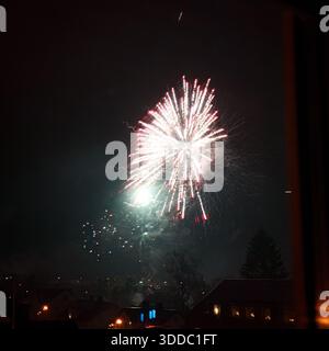 A vibrant firework burst illuminates the night sky over a quiet residential area. The image captures the moment of peak explosion with trails and smok Stock Photo
