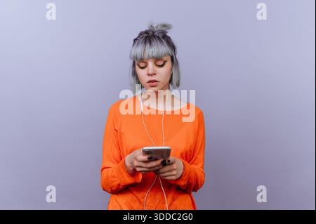 Young woman with headphones using smartphone against purple background. Stock Photo