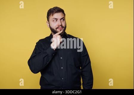 Man in black shirt thinking against yellow background Stock Photo