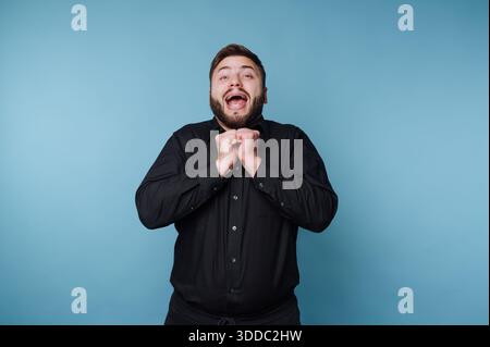 Man in black shirt expressing excitement against blue background Stock Photo