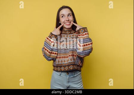 Woman in patterned sweater smiling against yellow background. Stock Photo