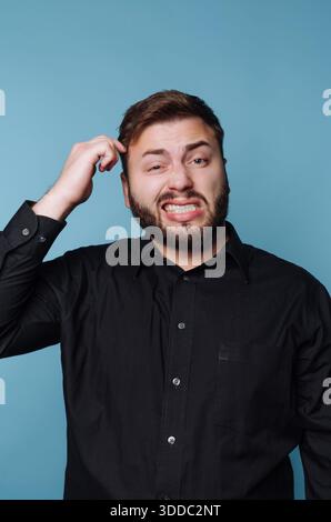 Man in black shirt scratching head with confused expression. Stock Photo