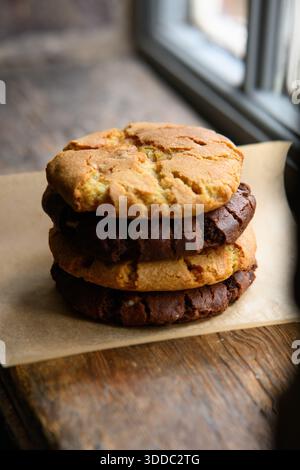 Three cookies stacked on top of each other on a wooden table. The cookies are different flavors, with one being chocolate and the other two being vani Stock Photo