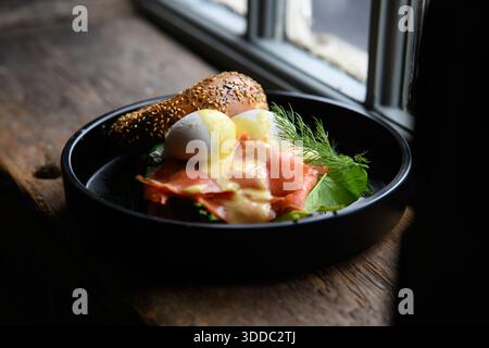 A plate of food with a sandwich and egg yolk on top. The plate is black and sits on a wooden table Stock Photo