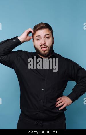 Man in black shirt scratching head with confused expression Stock Photo