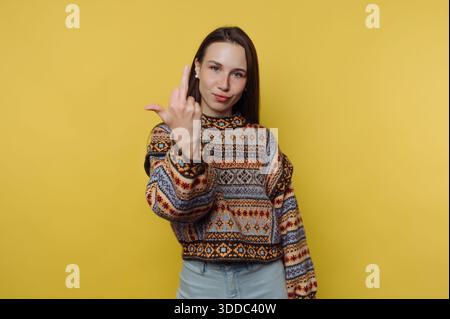 Woman in a patterned sweater making a rude gesture against a yellow background. Stock Photo