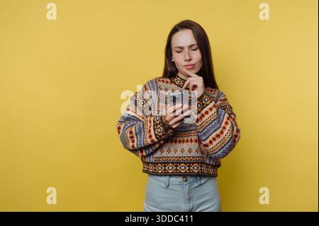 Woman in patterned sweater using smartphone against yellow background. Stock Photo